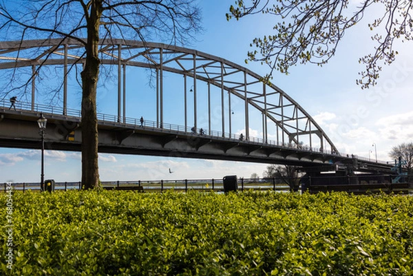 Obraz Arch bridge in Deventer seen from below with cyclists and walkers with greenery in the foreground and clear blue sky