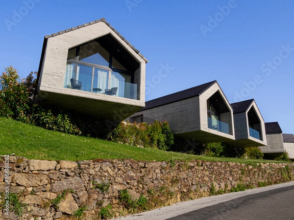Obraz Casas de lujo al pie de la carretera con balcones acristalados, soleadas cielo azul y césped verde con muro de piedra, en verano de 2021 en Galicia España.