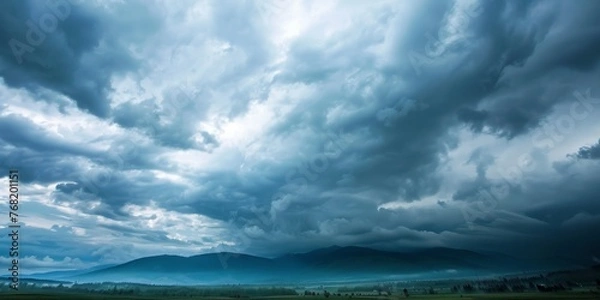 Fototapeta A field with mountains in the distance, set under a dramatic grey sky