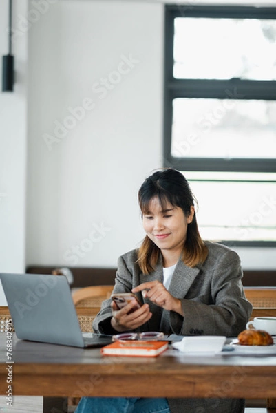 Fototapeta Businesswoman is interacting with her smartphone at her work desk, seamlessly switching between devices to maximize productivity.