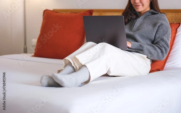 Fototapeta Closeup of a woman using and working on laptop computer while lying on bed