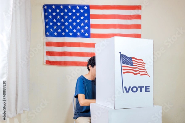 Fototapeta A man in the voting booth casting his vote to choose the new President of the United States. The polling location is adorned with American flags.