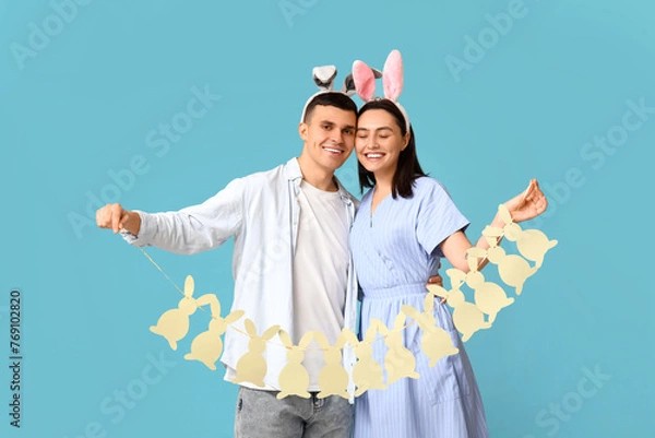 Obraz Happy young couple with Easter bunny ears and garland on blue background