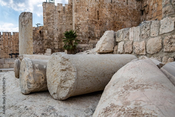 Fototapeta Dramatic image of ruins in front of the old city Jerusalem gates with weathered stone columns in the foreground.