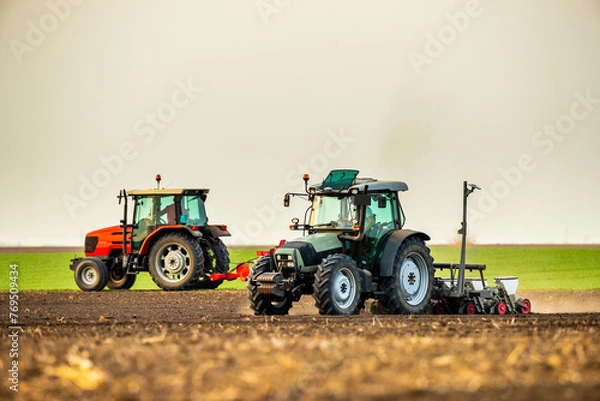 Fototapeta Two tractors plough and sow in tandem on a vast farm field
