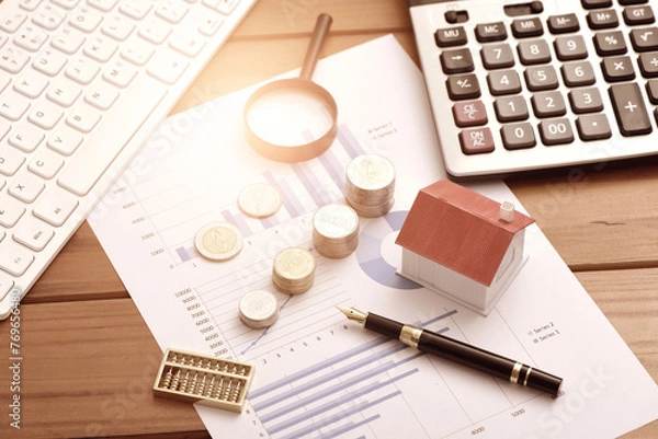 Obraz Small houses, coins, and office supplies placed on financial data reports