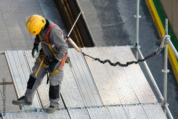 Obraz construction workers with safety equipment assembling scaffolding for maintenance of building facade on city street