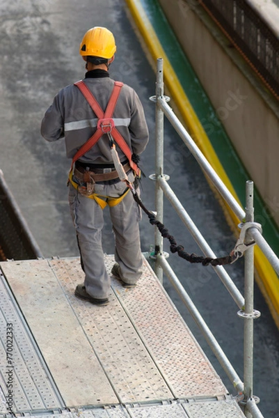 Obraz construction workers with safety equipment assembling scaffolding for maintenance of building facade on city street