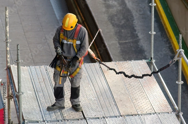 Obraz construction workers with safety equipment assembling scaffolding for maintenance of building facade on city street