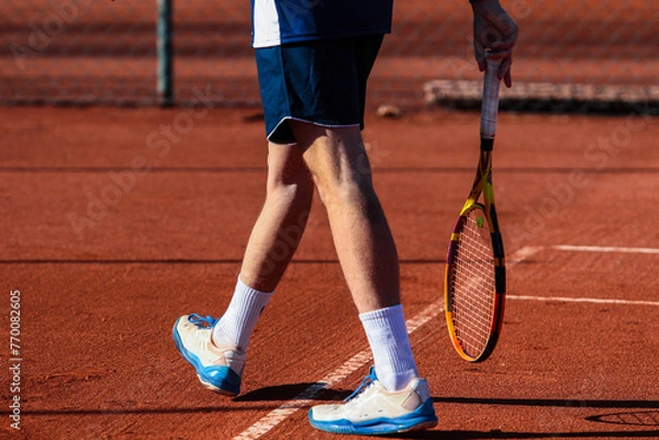 Obraz Close up of young boy with racket playing tennis on a clay court during a university tournament. the athlete is wearing a blue sports shirt.