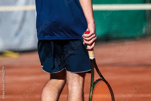 Obraz Close up of young boy with racket playing tennis on a clay court during a university tournament. the athlete is wearing a blue sports shirt.