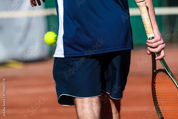 Obraz Detail of young boy with racket playing tennis on a clay court during a university tournament. the athlete is wearing a blue sports t-shirt and is preparing to serve for set point