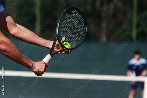 Obraz Detail of young boy with racket playing tennis on a clay court during a university tournament. the athlete is wearing a blue sports t-shirt and is preparing to serve for set point