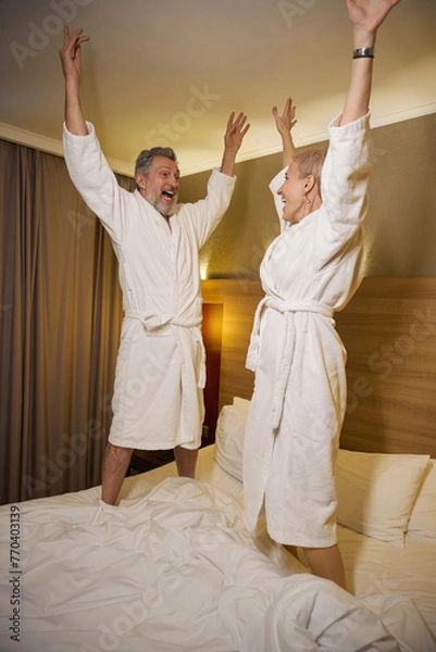 Fototapeta Joyful couple with hands in air celebrating and looking at each other on bed