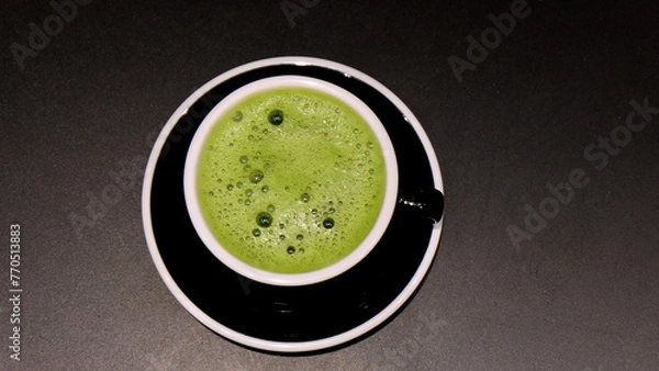 Obraz Closeup of a cup of matcha green tea drink, with some froth on the top. With a black cup and a black background.