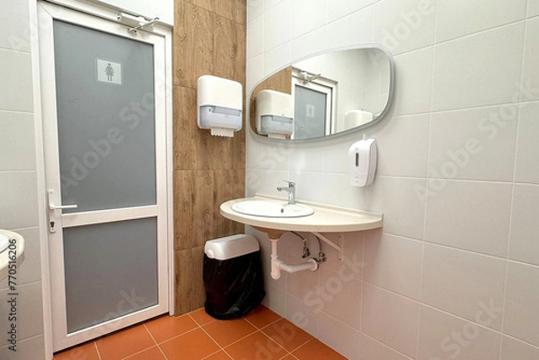 Obraz single sink in small public toilet with wall soap dispenser and paper towlels