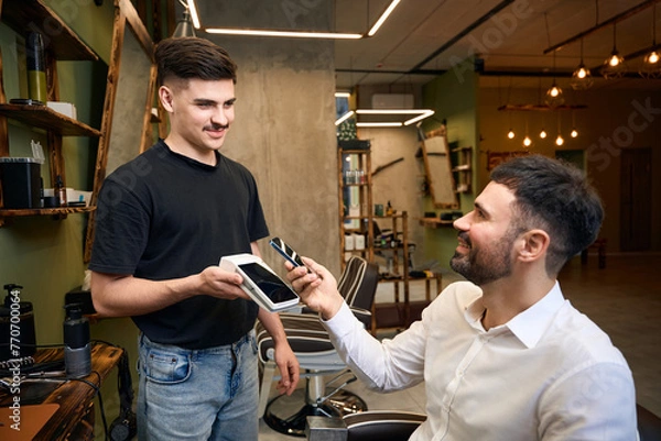 Fototapeta Client paying in barbershop with smartphone and pos terminal