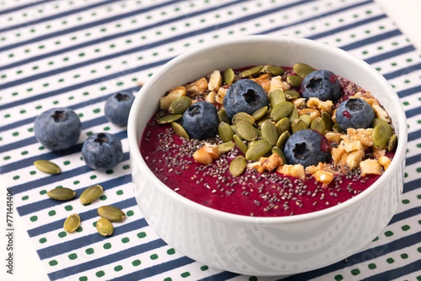 Fototapeta Mixed berry smoothie in a white bowl bowl topped with blueberries, pumpkin seed, walnuts and chia seed