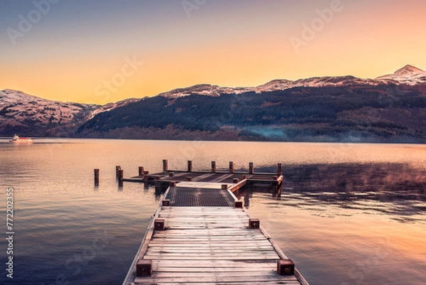 Fototapeta A pier extending over the calm waters of Loch Lomond at sunrise in Scotland