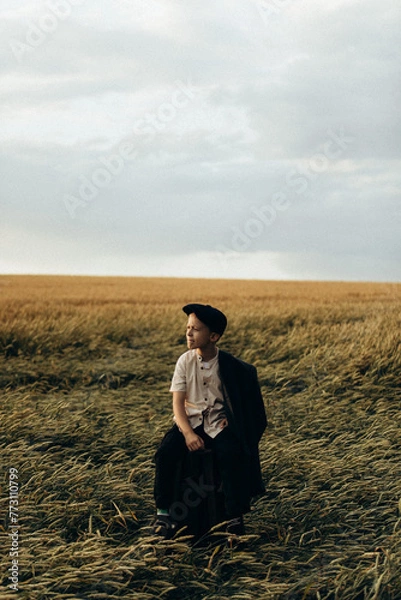 Obraz a village boy sits on a chair in the middle of a wheat field and looks away