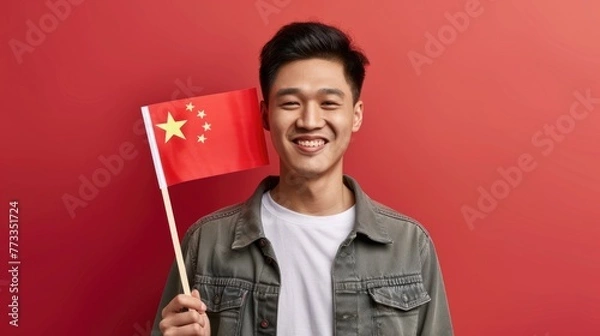 Obraz A smiling young man is holding a Chinese flag against a red background