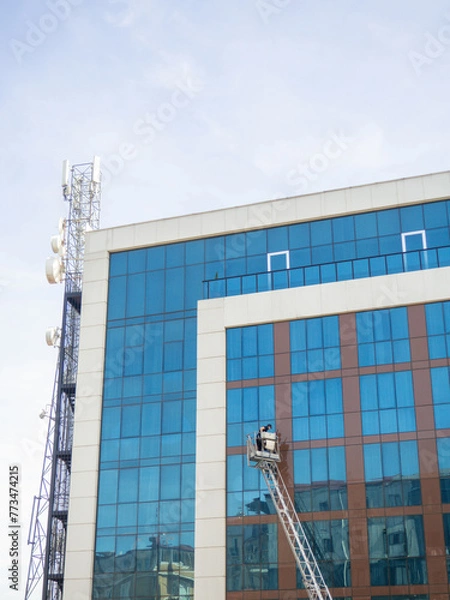Fototapeta Cleaning windows in a large glass building. Work at height on a lift. Man in a cradle.