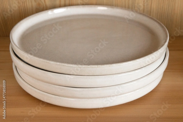 Fototapeta A stack of beige ceramic plates in a wooden cupboard.