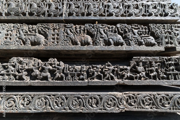 Fototapeta Ornate carvings of a war scene on a panel on the stone wall of the ancient Hoysaleshwara temple in Halebeedu.
