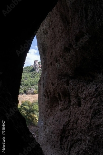 Obraz Vertical view out of a cave with green hills in the background on a sunny day