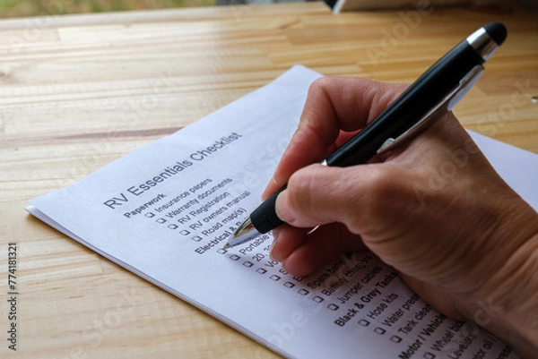 Fototapeta Hand holding a pen checking off boxes on RV Essentials Checklist