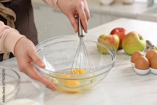 Obraz Woman whisking eggs in bowl at light marble table indoors, closeup