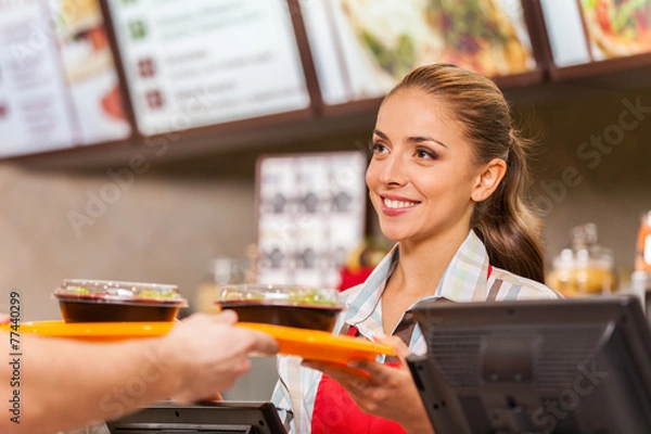 Obraz Pracownik restauracji obsługujący dwa posiłki typu fast food z uśmiechem.