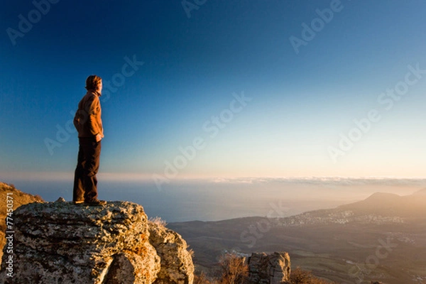 Obraz man on the cliff in mountains at sunset