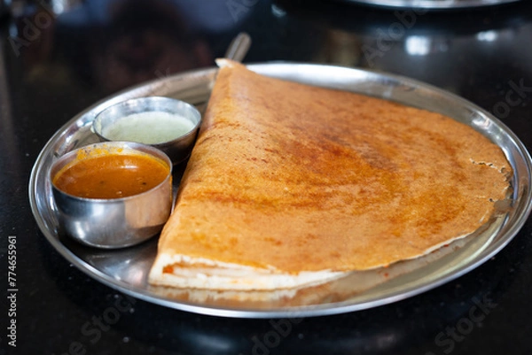 Fototapeta A delicious, crispy dosa served with savory sambar and coconut chutney on a stainless steel plate, capturing the essence of South Indian cuisine.