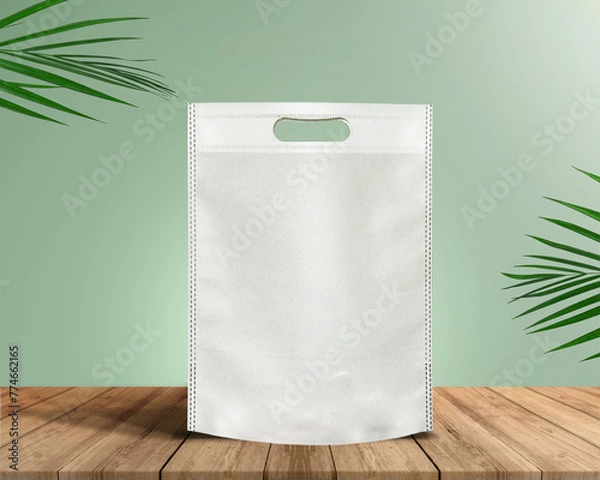 Fototapeta White Color Eco Friendly Tote Bag With Loop Strap. Non Woven Fabric Bag isolated on wood table with plants green background With copyspace for text