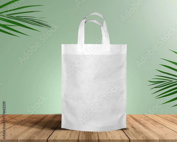 Fototapeta White Color Eco Friendly Tote Bag With Loop Strap. Non Woven Fabric Bag isolated on wood table with plants green background With copyspace for text