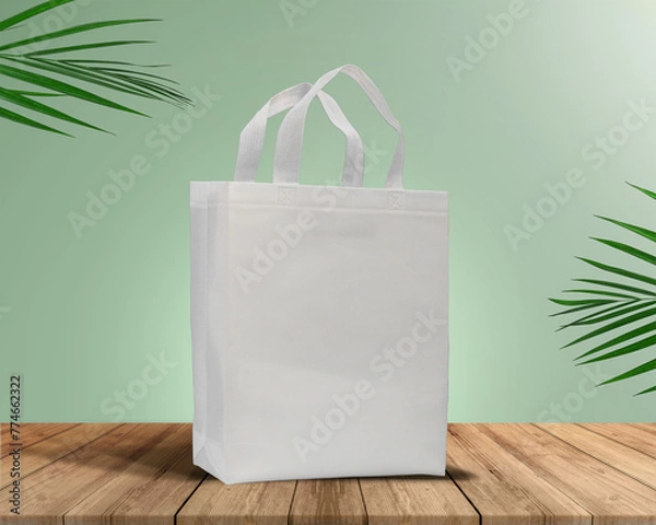 Fototapeta White Color Eco Friendly Tote Bag With Loop Strap. Non Woven Fabric Bag isolated on wood table with plants green background With copyspace for text