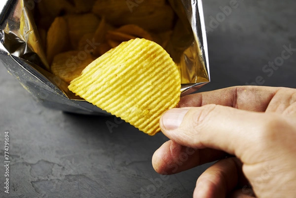 Fototapeta A hand takes potato chips from a pack