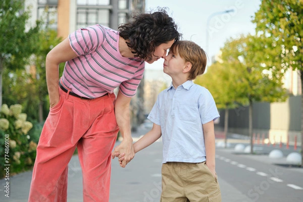 Obraz Adorable mother and son smiling happy having fun at city background. Motherhood concept, hugging. Boy 8 years old with mother in bright clothes enjoying summer day. High quality photo