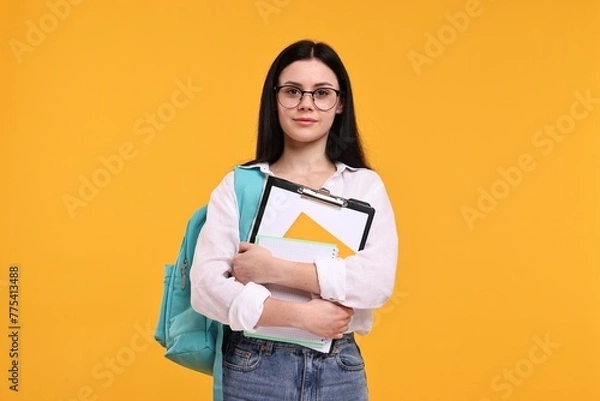 Fototapeta Student with notebooks and clipboard on yellow background