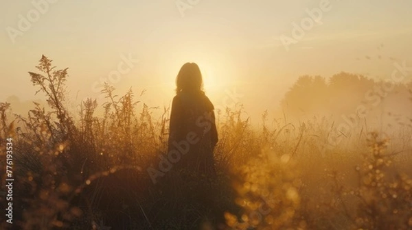 Fototapeta A woman standing alone on the grass with a sunset in the background AI generated image
