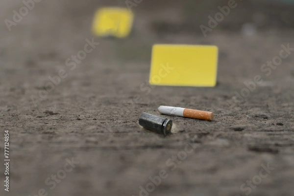 Fototapeta Pistol bullet shell on cement floor with blurred yellow paper and cigarette filter scraps background, concept for investigation and crime by police officers and investgators, soft focus.
