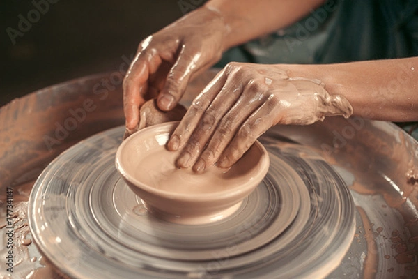 Obraz A person is making a bowl out of clay. The bowl is in the center of the image and the person is using their hands to shape it. The bowl is not yet finished