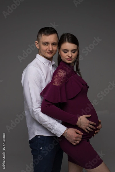 Obraz portrait of a pregnant couple, pregnant couple stands on a grey background in a studio, studio pregnancy photo shoot, pregnant woman posing in a studio, pregnant, pregnancy