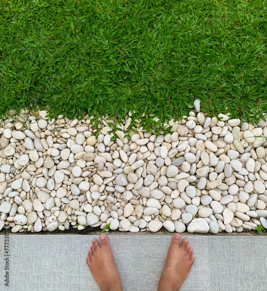 Obraz Feet on Fresh Green Grass with White Pebbles, Bare feet on grass, concept of relaxation and connection with nature