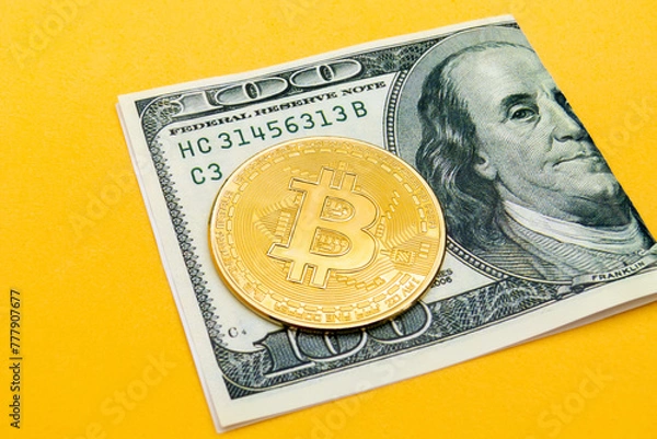 Obraz a folded one hundred dollar bill with a bitcoin cryptocurrency on top, focusing on the currency from an inclined and elevated angle on a yellow background, concept of web3 exchange and blockchain