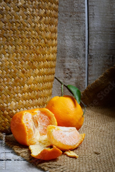 Fototapeta Tangerines or mandarin oranges (Citrus reticulata) are oranges that can grow in tropical and subtropical areas, randomly some are whole, some have been cut, with a natural wood and woven background