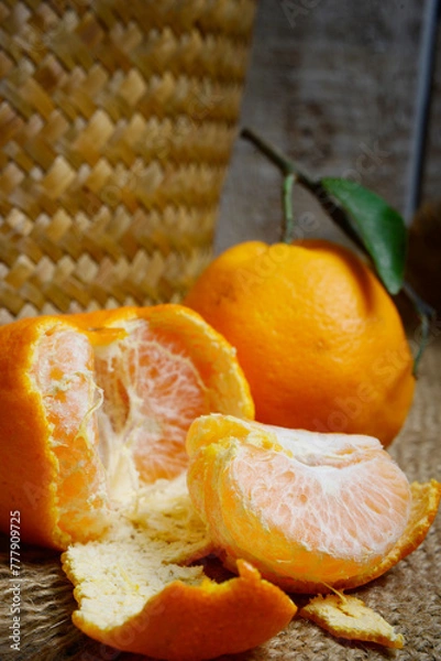 Fototapeta Tangerines or mandarin oranges (Citrus reticulata) are oranges that can grow in tropical and subtropical areas, randomly some are whole, some have been cut, with a natural wood and woven background