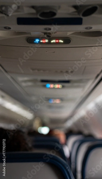 Fototapeta Lit up airplane no smoking and fasten seatbelts signs on a plane with passengers.