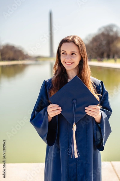 Obraz Young woman graduate holding a cap, smiling with a reflecting pond and Washington Monument in the background.